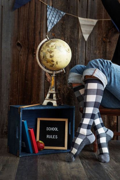 Lower legs of a model in Lunatik Ivory Lumber Jack compression socks (checkered pattern) in front of a globe and some textbooks.