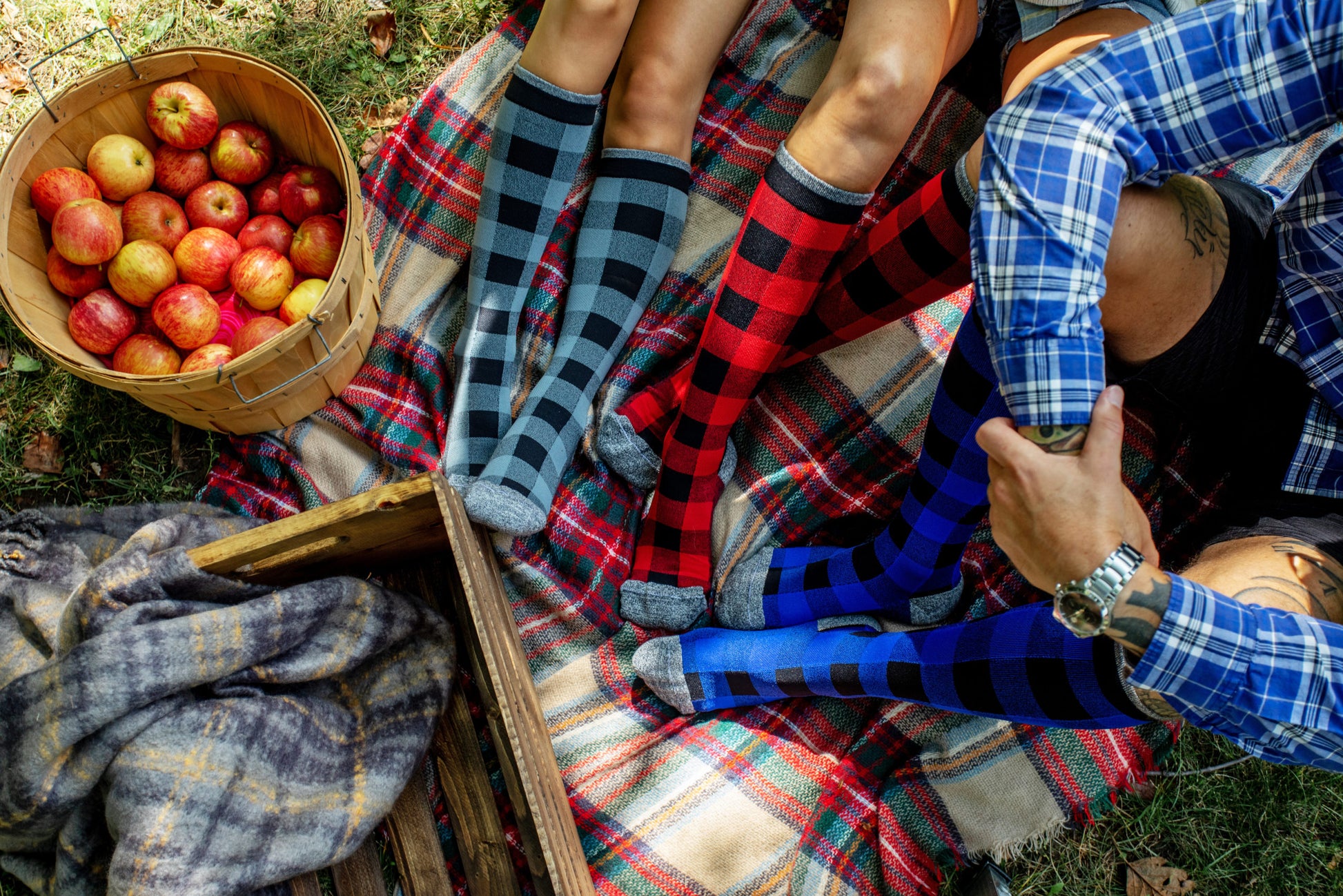 Three friends on a picnic mat wearing Lunatik Lumber Jack compression socks in grey, red, and blue.