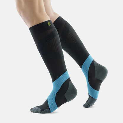 Lower legs of a model in black and blue Bauerfeind training compression socks standing in front of a white background.