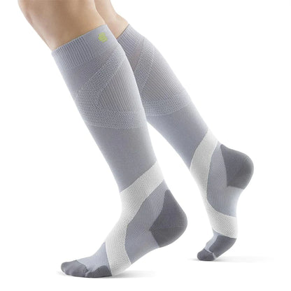 Lower legs of a model in silver polar Bauerfeind training compression socks standing in front of a white background.