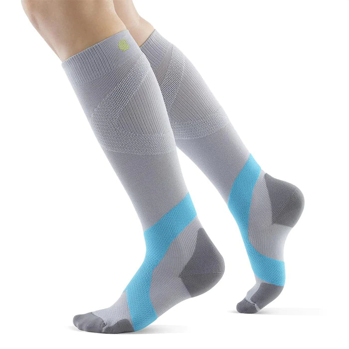 Lower legs of a model in silver rivera Bauerfeind training compression socks standing in front of a white background.