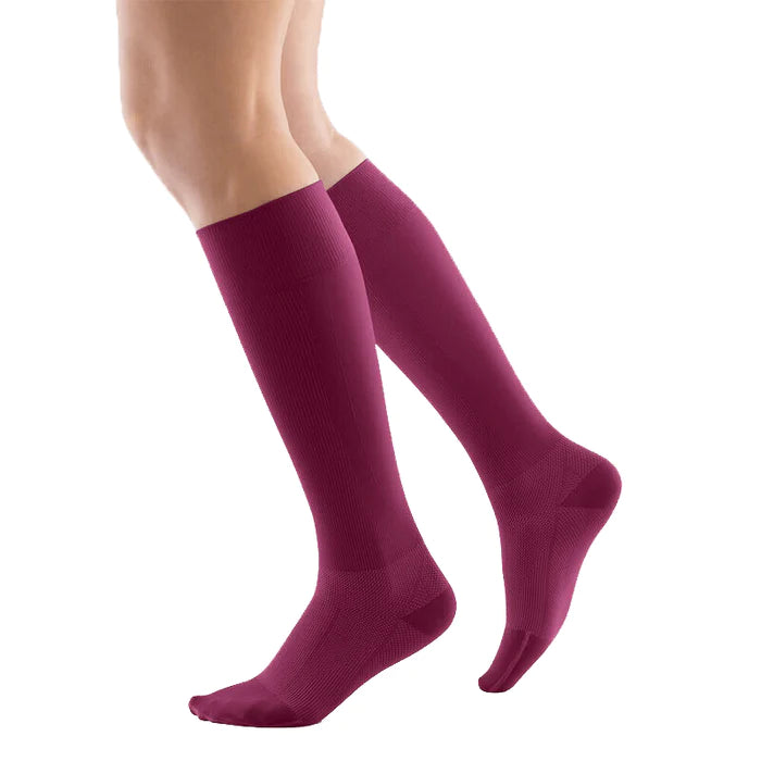 Lower legs of a model in berry Bauerfeind performance compression socks standing in front of a white background.