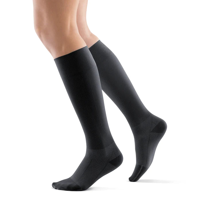 Lower legs of a model in black Bauerfeind performance compression socks standing in front of a white background.