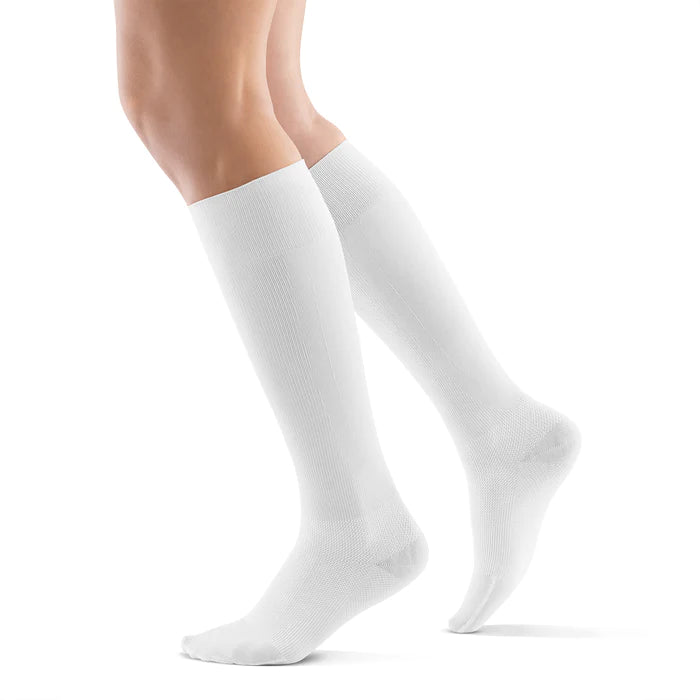 Lower legs of a model in white Bauerfeind performance compression socks standing in front of a white background.