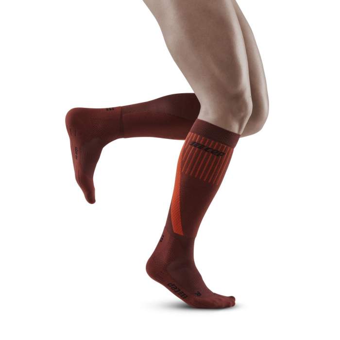 Lower legs of male model running in knee-high CEP Cold Weather compression socks in dark orange.