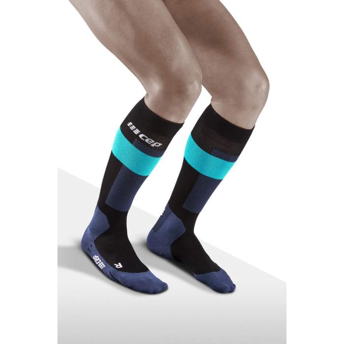 Lower legs of model crouching in knee-high CEP Merino skiing compression socks in blue, turqoise and black accents.