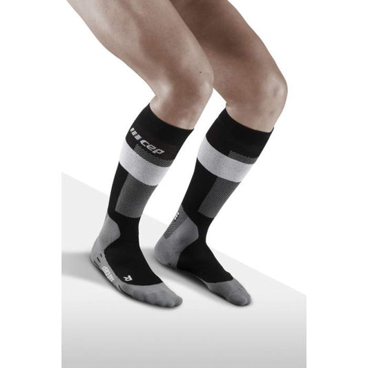 Lower legs of model crouching in knee-high CEP Merino skiing compression socks in grey, black accents.