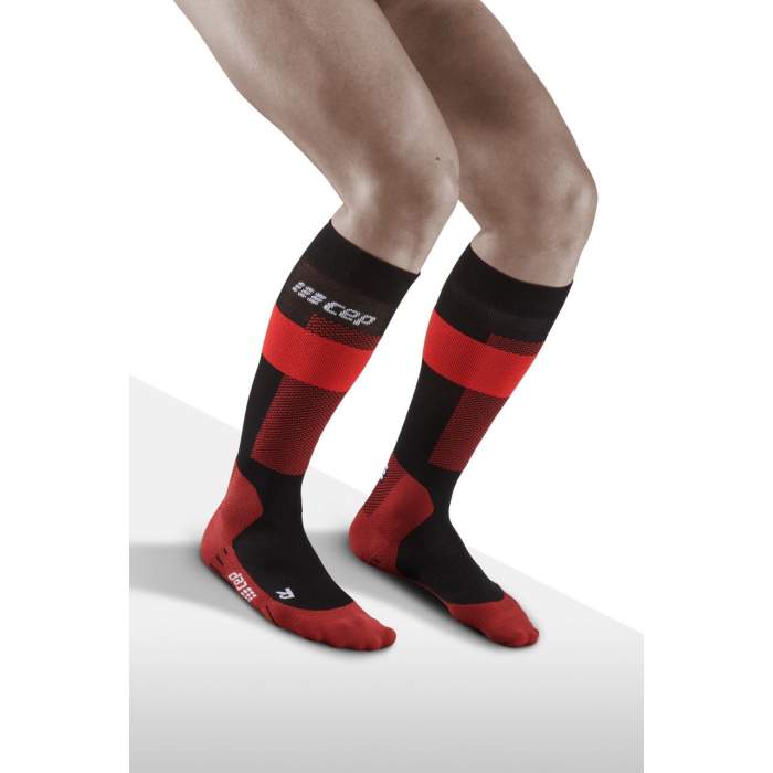 Lower legs of model crouching in knee-high CEP Merino skiing compression socks in red, black accents.