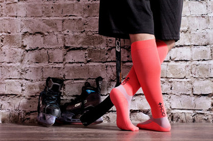 Lower legs of ice hockey player in Lunatik Vibe Tech compression socks in pink.