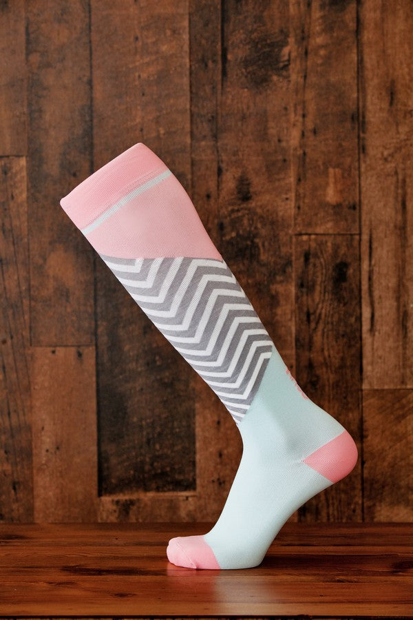 Light pink and pale blue Lunatik Bofa Tech compression socks on wooden floor and background.