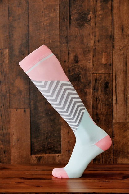 Light pink and pale blue Lunatik Bofa Tech compression socks on wooden floor and background.