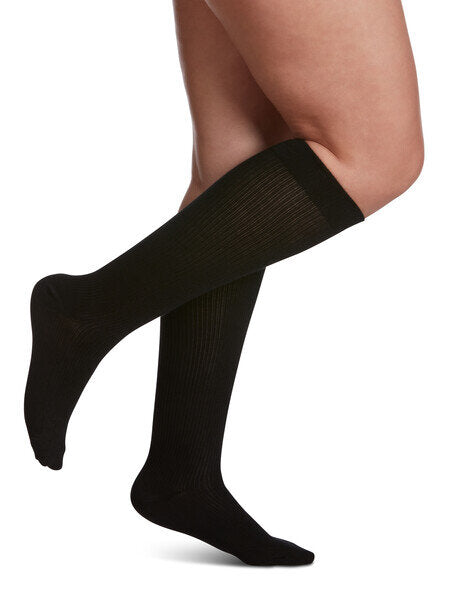 Legs of model in black Sigvaris Casual Cotton compression socks on white background.